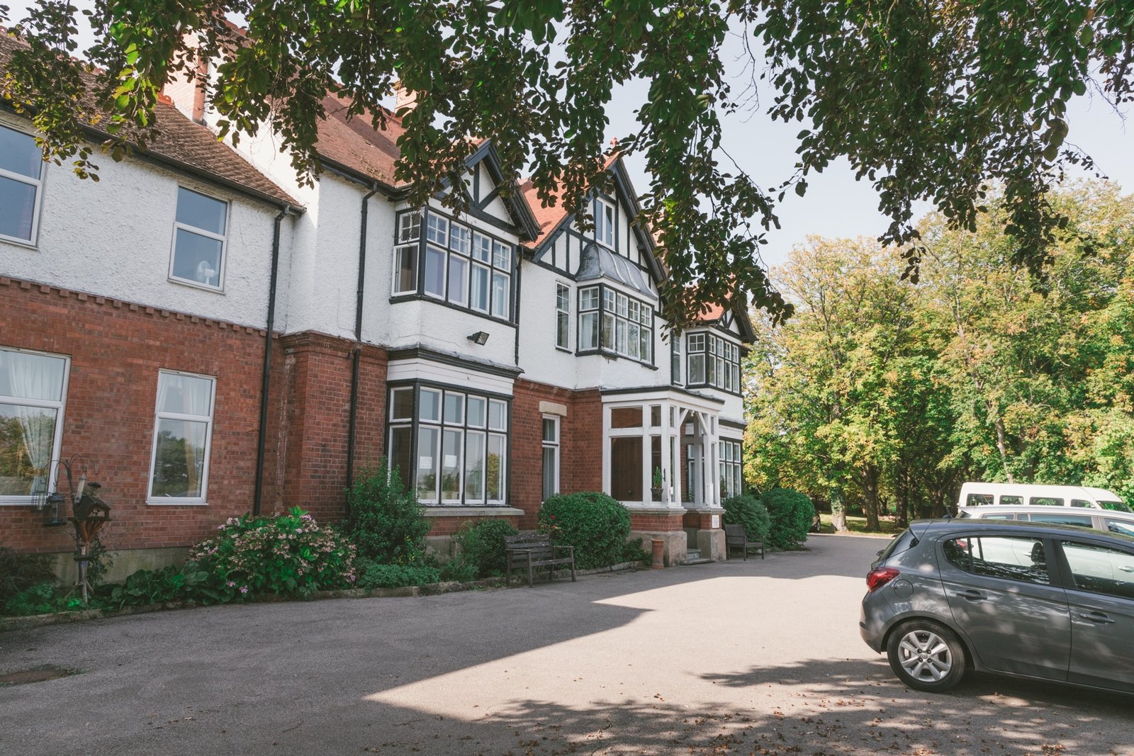 Traditional red-brick care home building surrounded by mature trees and gardens