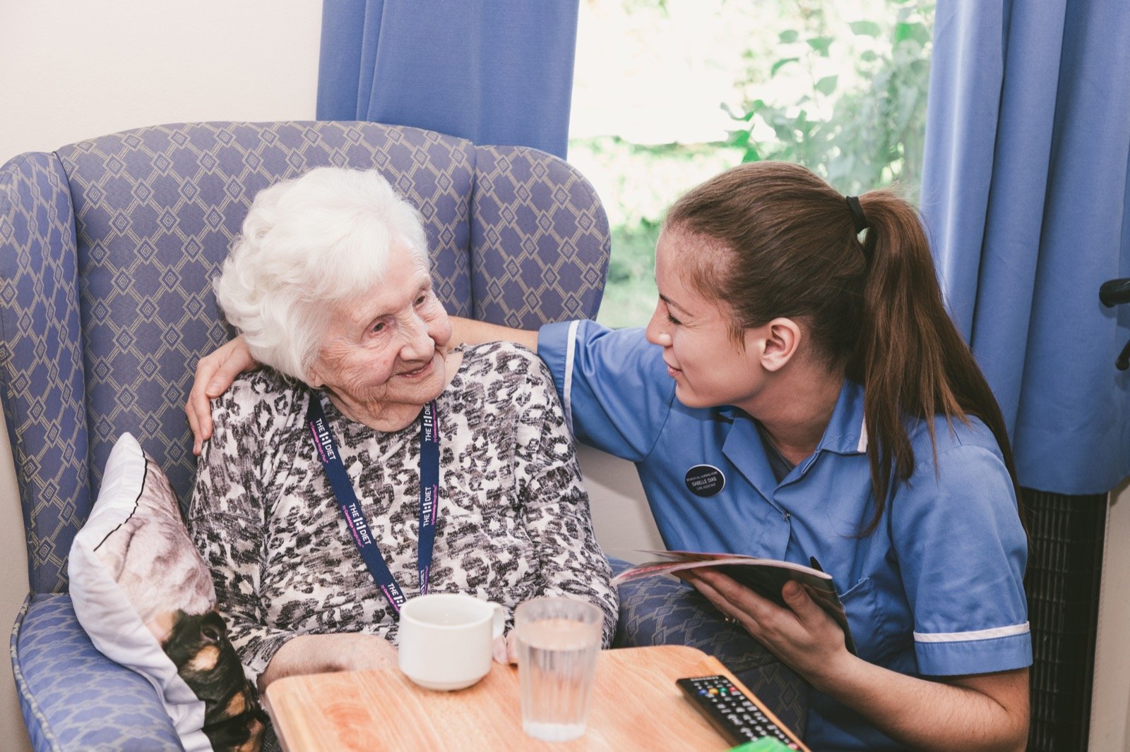 A resident sharing a magazine with a member of care staff, both smiling