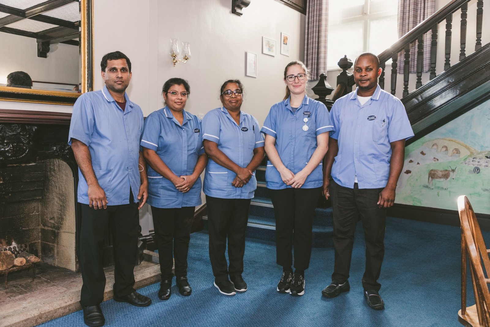 A group of five care home staff members smiling together in a communal hallway